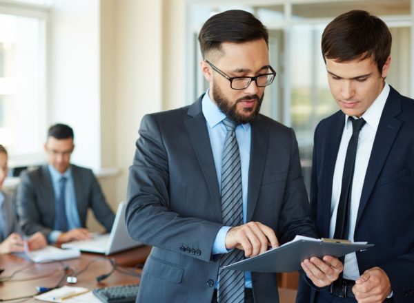 Paperwork Confident businessman pointing at document while explaining his idea to his partner on background of their colleagues